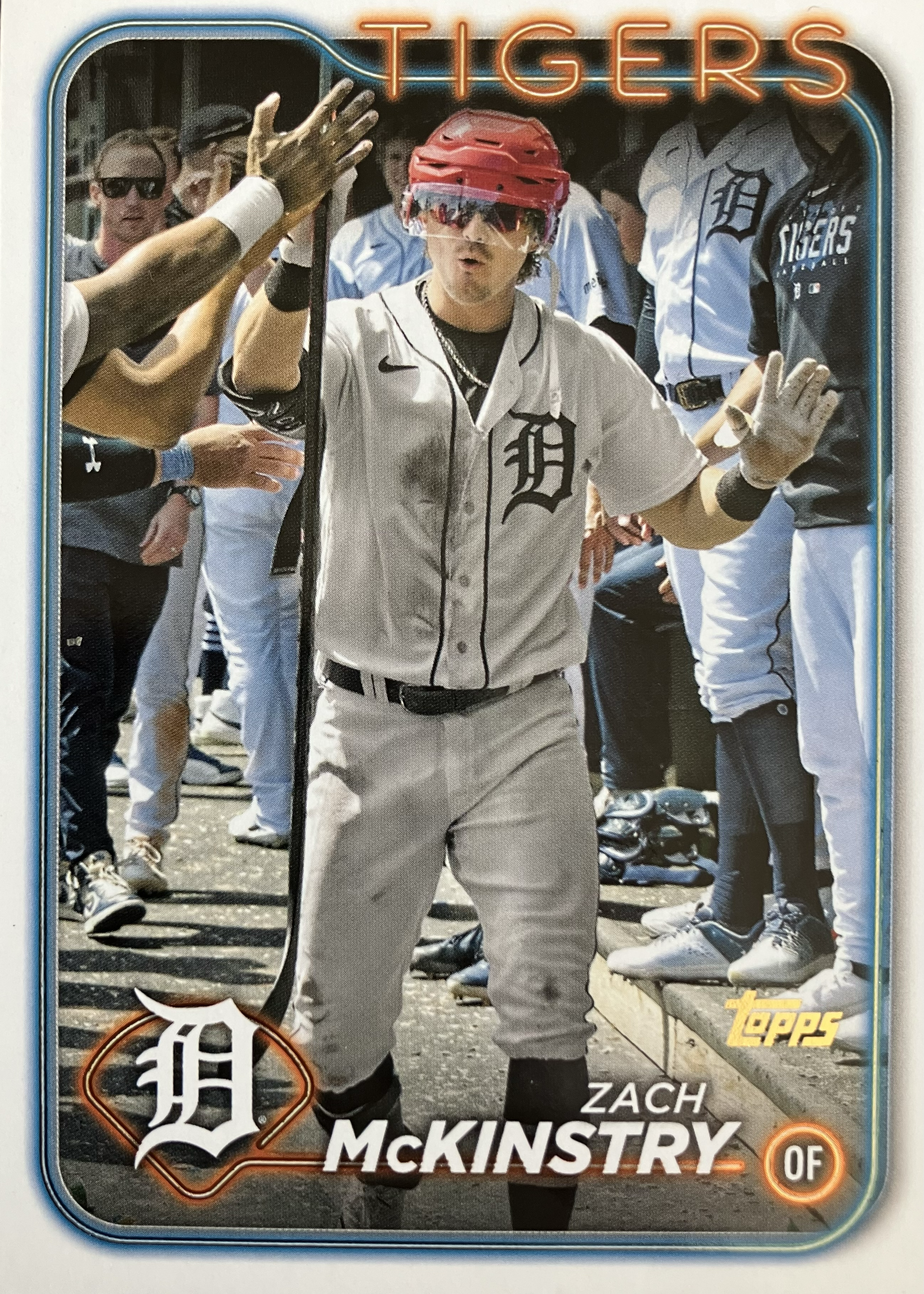 A baseball player carries a hockey stick, wearing a hockey helmet in the dugout.
